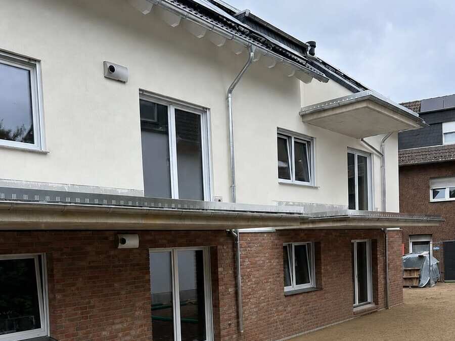 Fertiggestellter Neubau von außen: zweigeschossiges Wohnhaus mit Klinkersockel, verputztem Obergeschoss, auskragendem Vordach und Photovoltaik auf dem Dach, davor die angelegte Außenanlage im Kreis Euskirchen